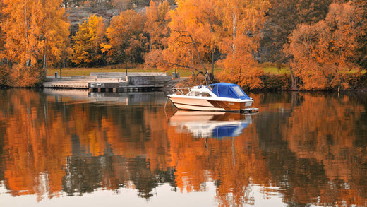 A boat sitting in a calm lake against a background of fall folliage.