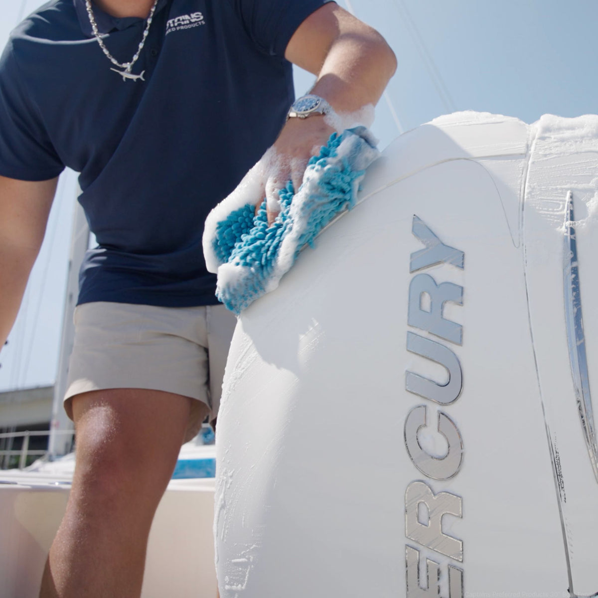 Person cleaning a boat engine with a blue wash mitt, wearing a navy shirt with a Captains Preferred Products logo.