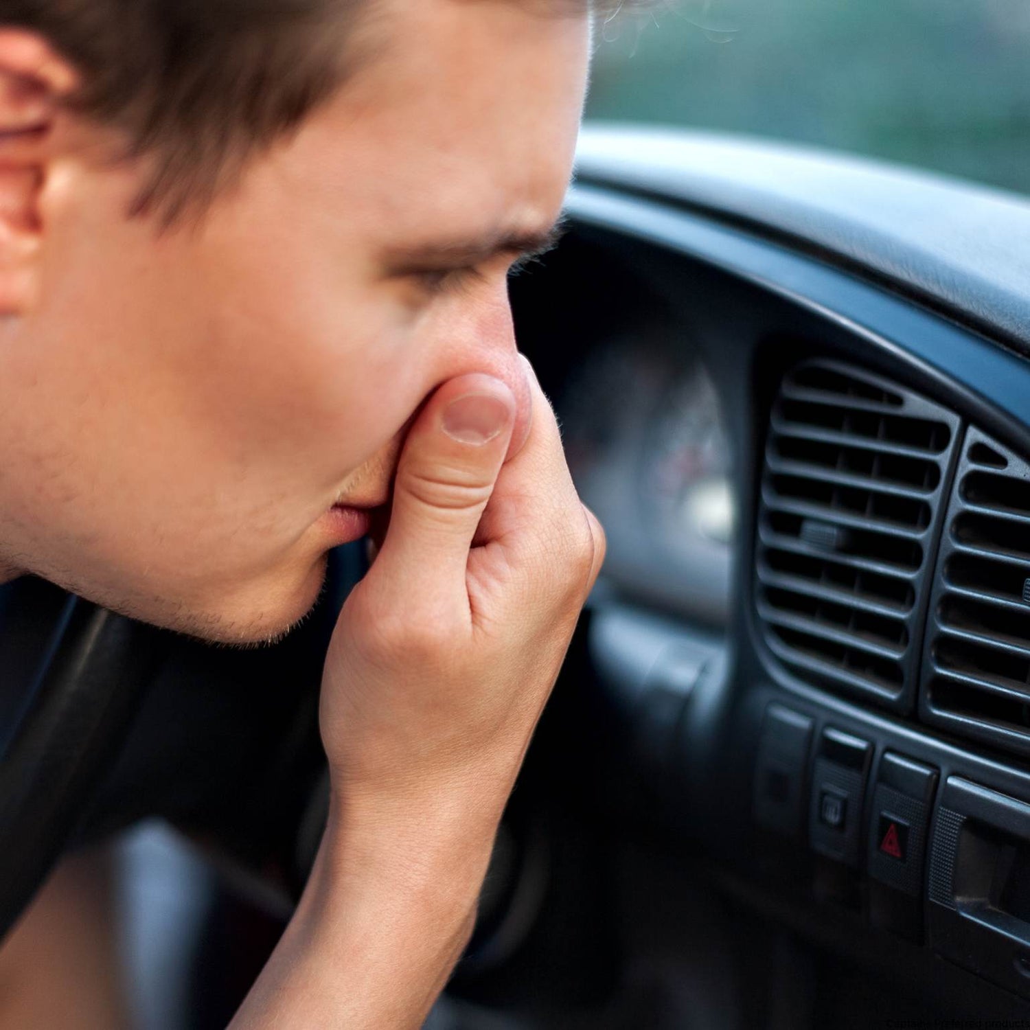 A man near his car vents holds his nose from a bad smell.