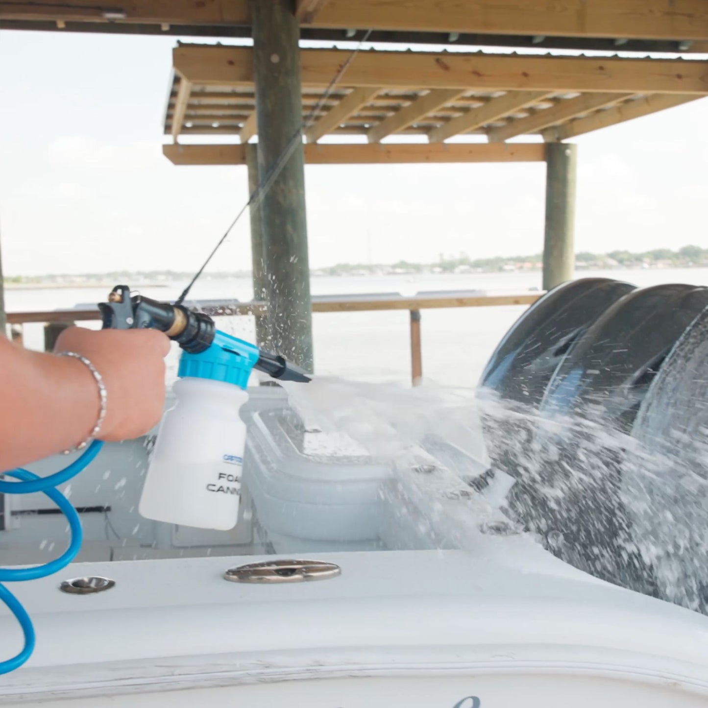 A foam cannon spraying foam on motor cowlings of a boat.