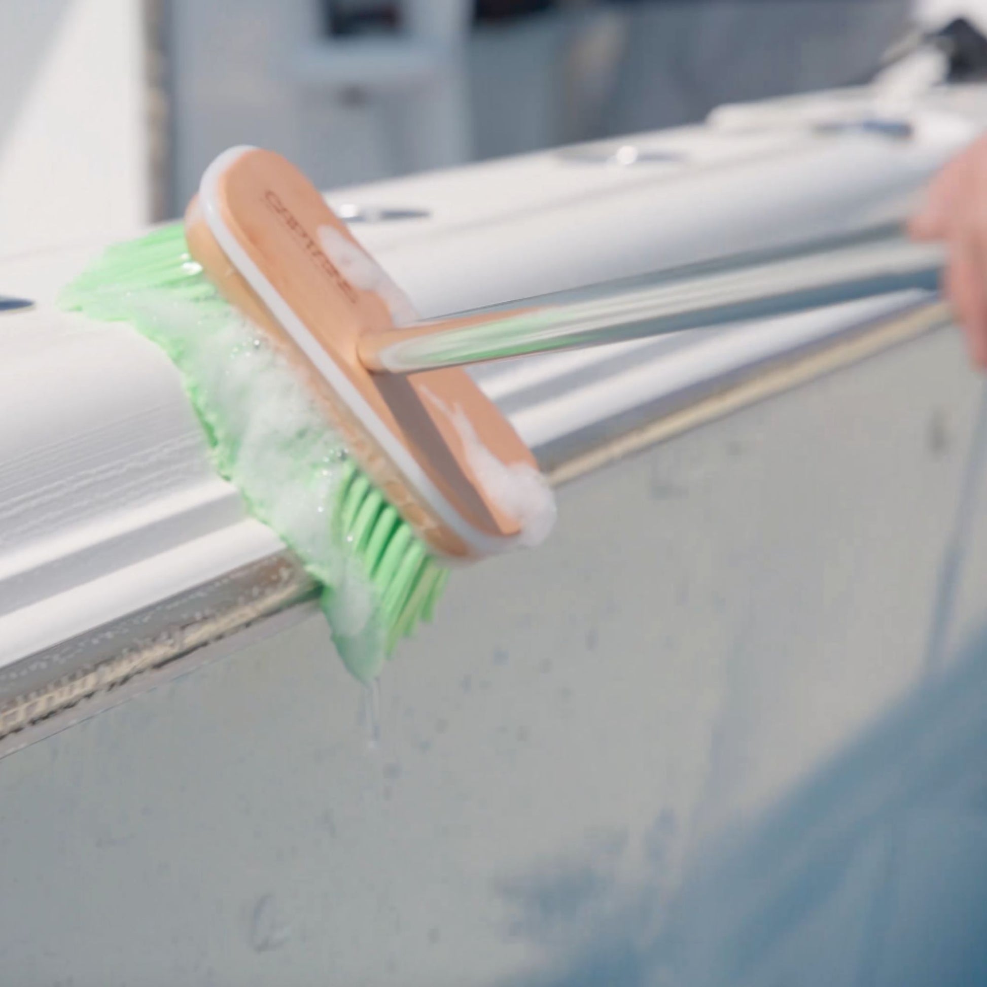 A green boat brush with suds cleans the side of a boat.