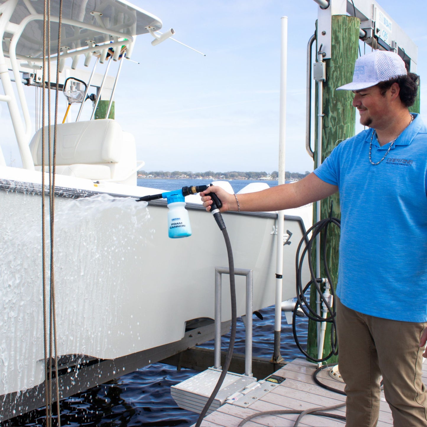 Man cleaning a boat with a foam cannon on a dock.