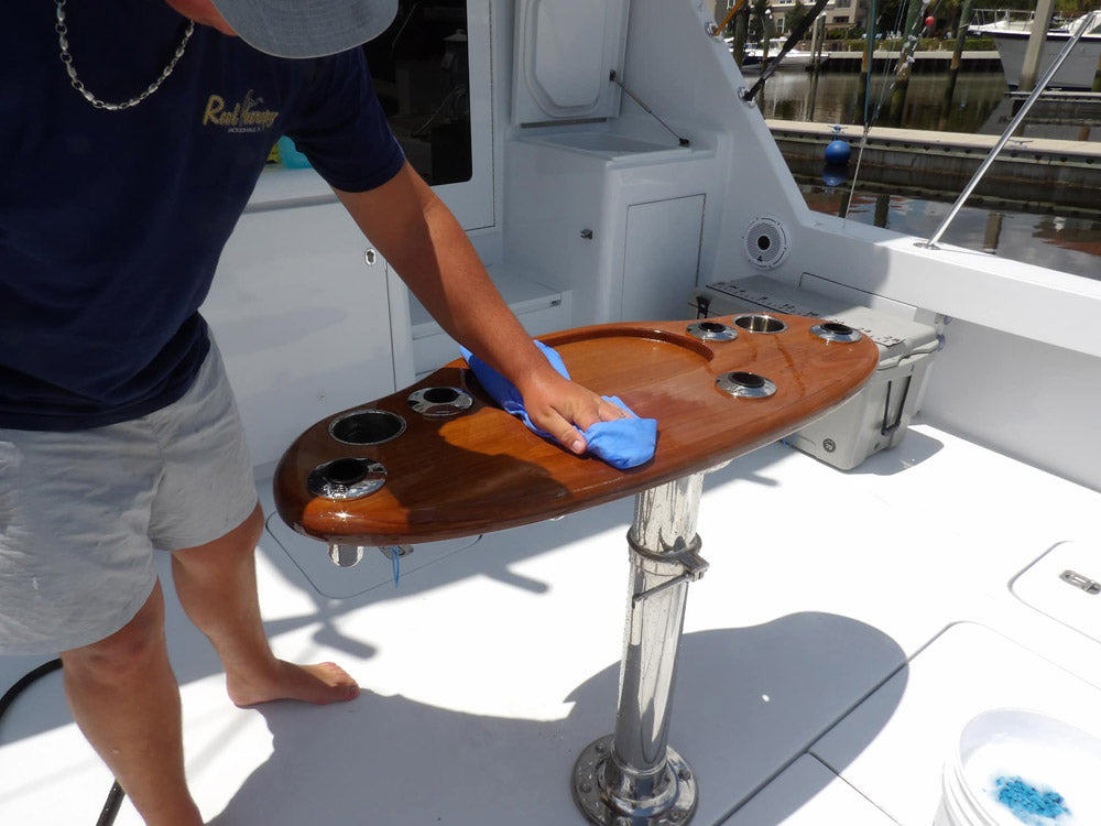A man uses a shammy towel to dry the console on the back of a boat.