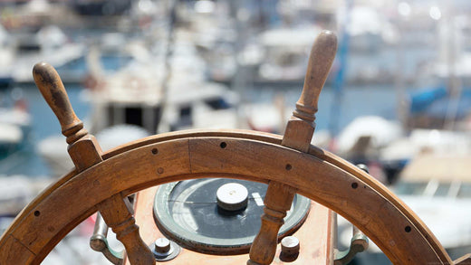 A spoked wooden boat wheel with a marina in the background.