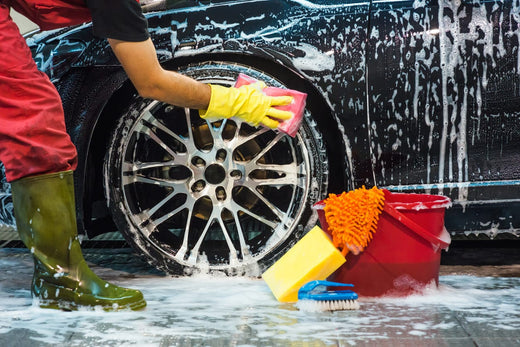 A person washing a soapy car with a sponge.