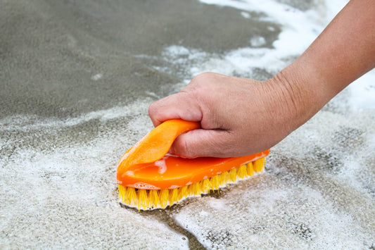 A hand holds a scrub brush cleaning carpet on a boat.