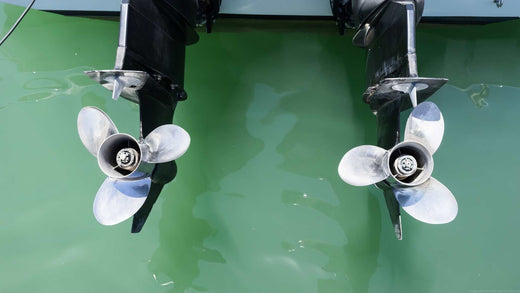 Two propellers extending from the back of a boat over green water.