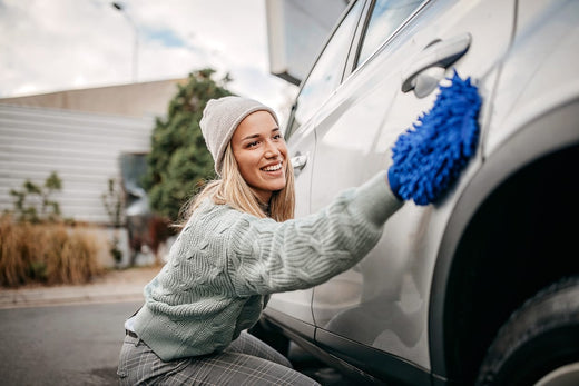 A woman using a blue wash mitt on a car.