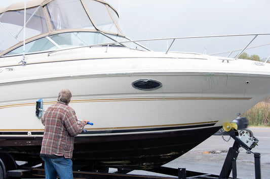 A man in a plaid shirt uses a scrub brush to clean the hull of a boat that has been taken out of the water.
