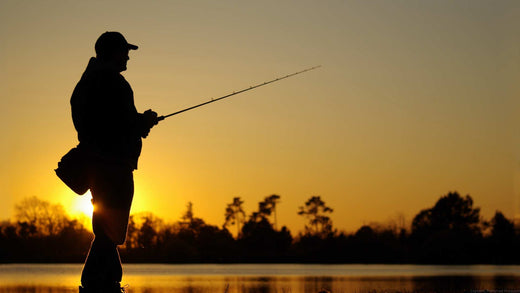 The silhouette of a professional fisherman holding a rod against a rising sun.