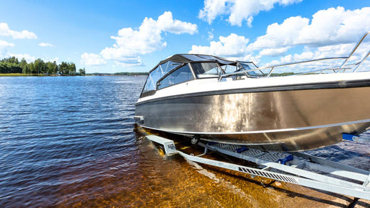 An aluminum lake boat being pulled out of the lake by a trailer.