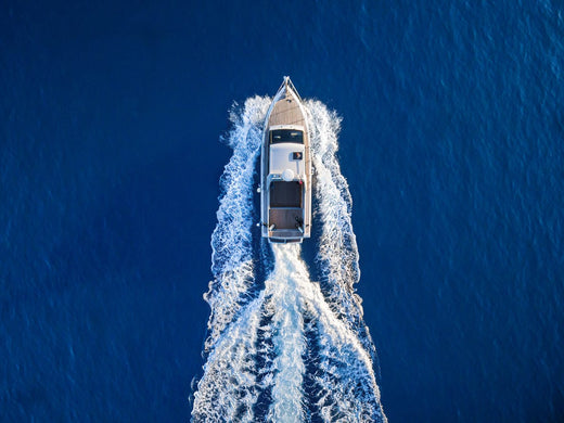 An aerial view of a boat cutting through a deep blue ocean.