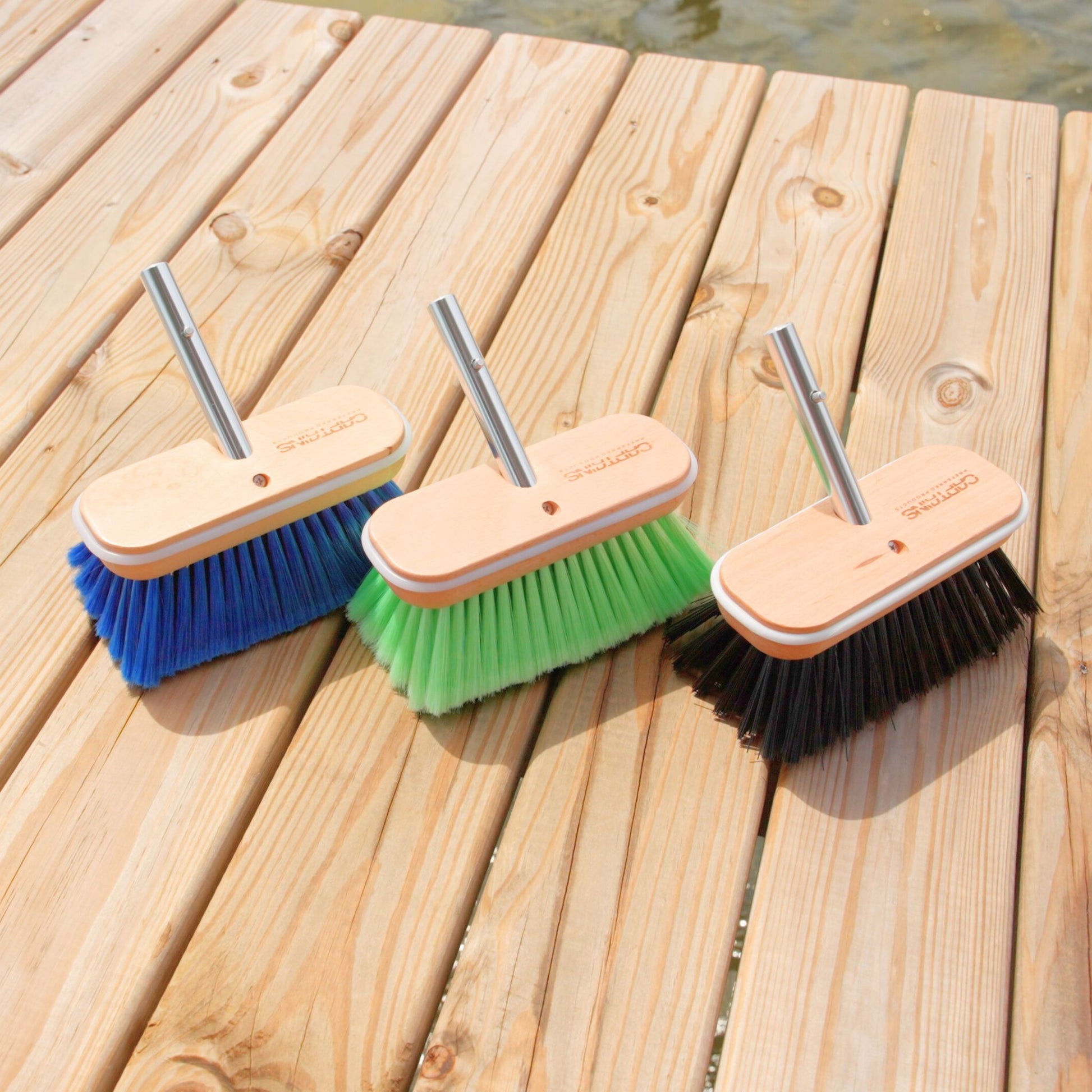 Three boat brush heads of different bristle hardnesses sitting on a boat dock.