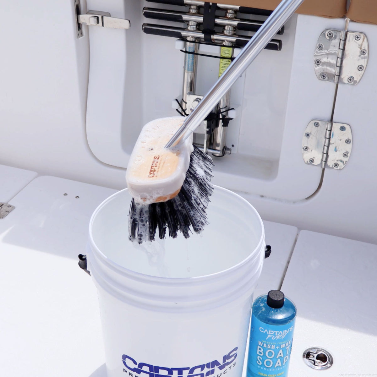A black hard bristled boat brush is dunked into a bucket of soapy water to clean a boat deck.