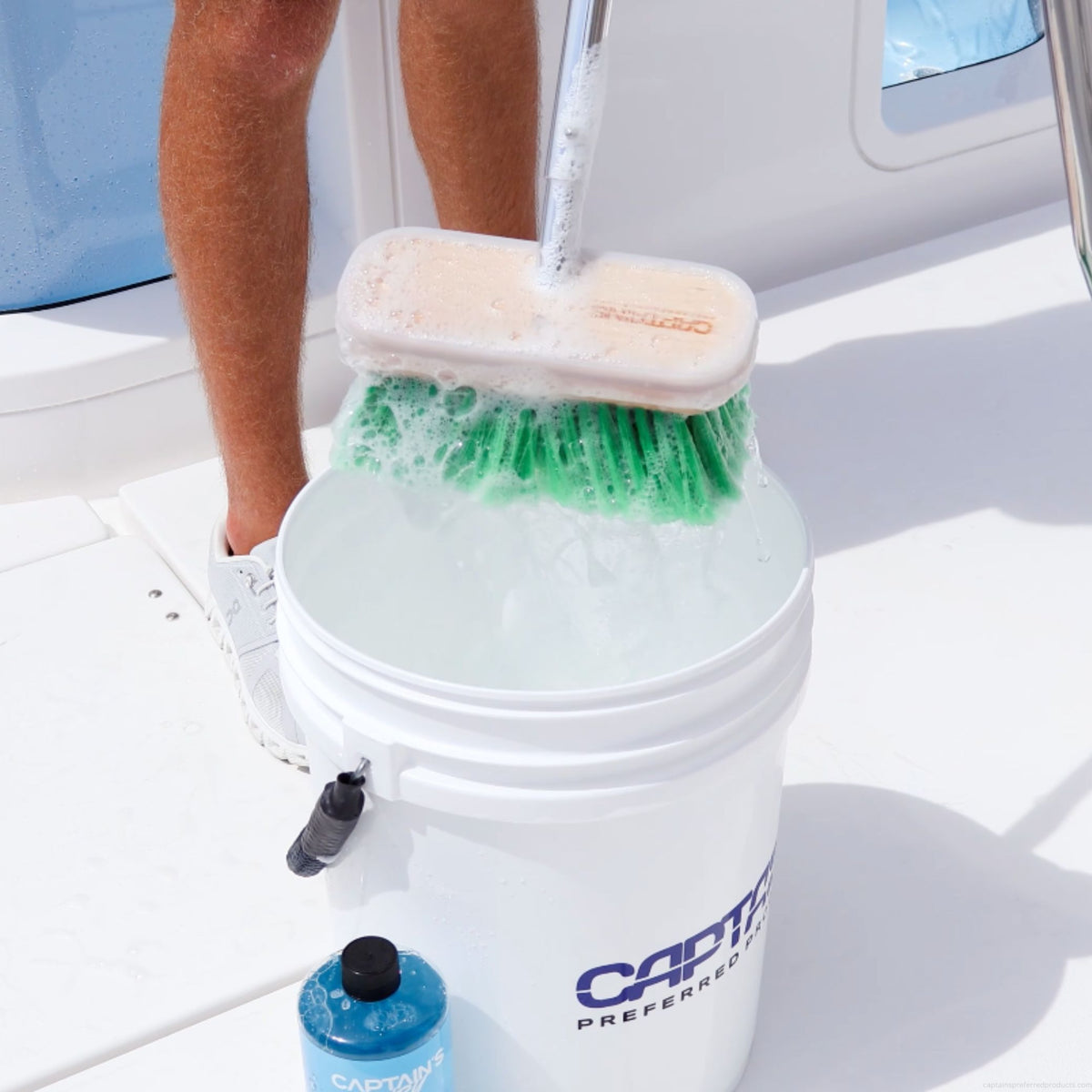 A green boat brush with medium bristles is dunked into a soapy bucket to clean a boat.