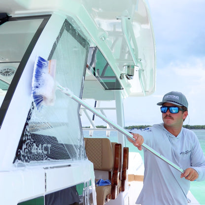 A man uses a blue soft boat brush to clean glass on a boat.