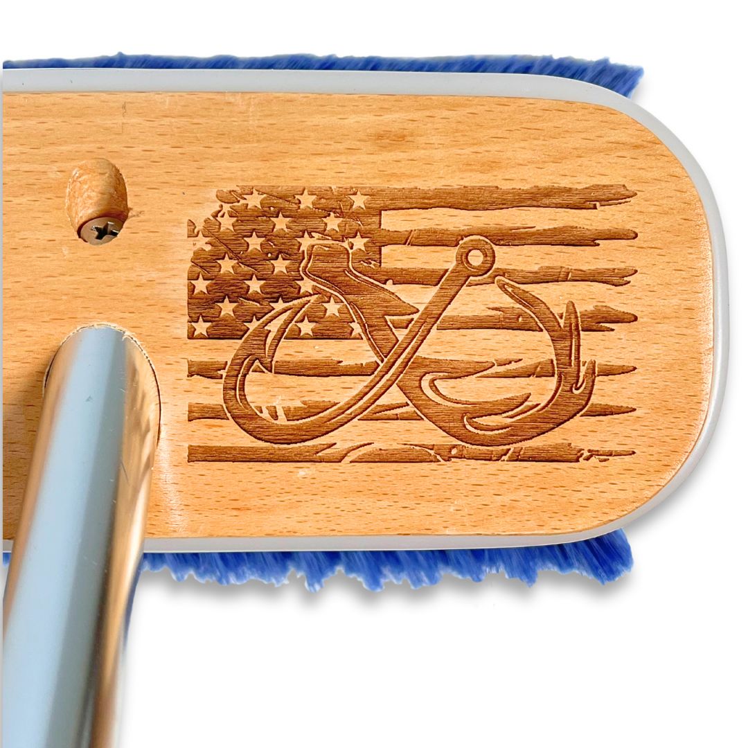 A fish hook, deer antler, and American flag design laser-etched into a wooden deck brush.