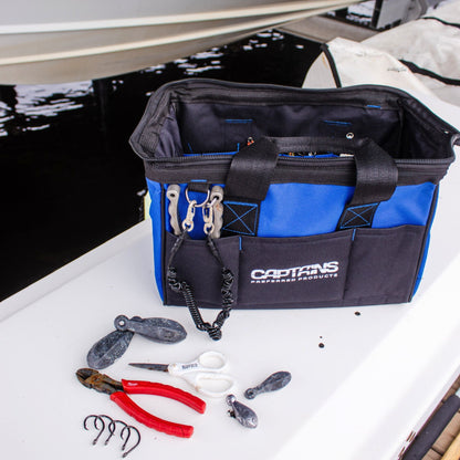 A fishing tool bag sits on the edge of a dock with tools and fishing gear around it.