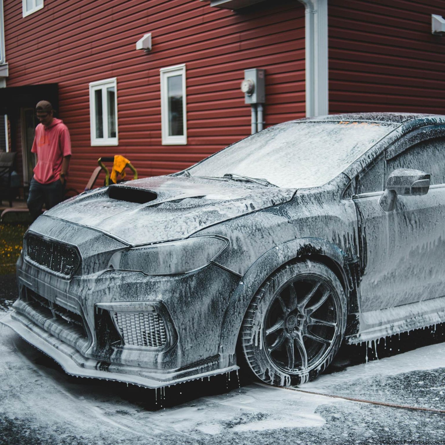 A black car covered in clinging foamy soap during a car wash.