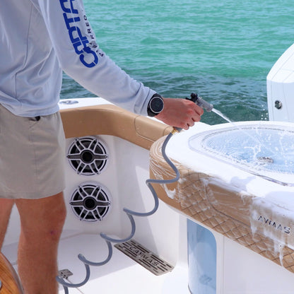 A man rinses soap of his boat with a gray hose while on the water.