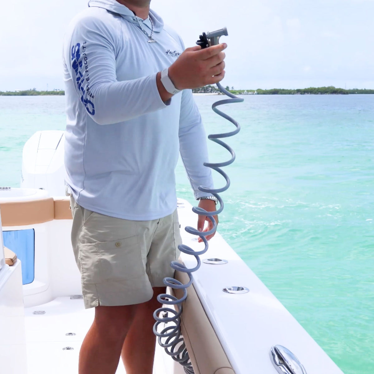 A man holds a coiled gray boat hose while out on the water.