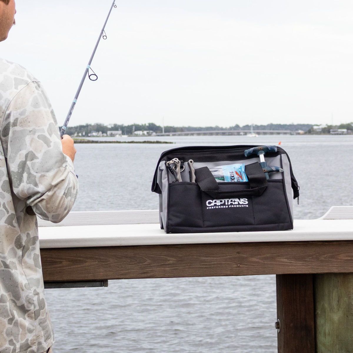 A gray fishing weight lead bag sits on the dock as a fisherman casts a line.