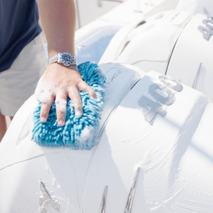 Person cleaning a white Mercury motor cowling with a blue microfiber wash mitt.