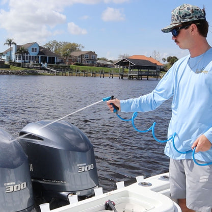 A man spraying a washdown hose with blue plastic nozzle at boat motor cowlings.