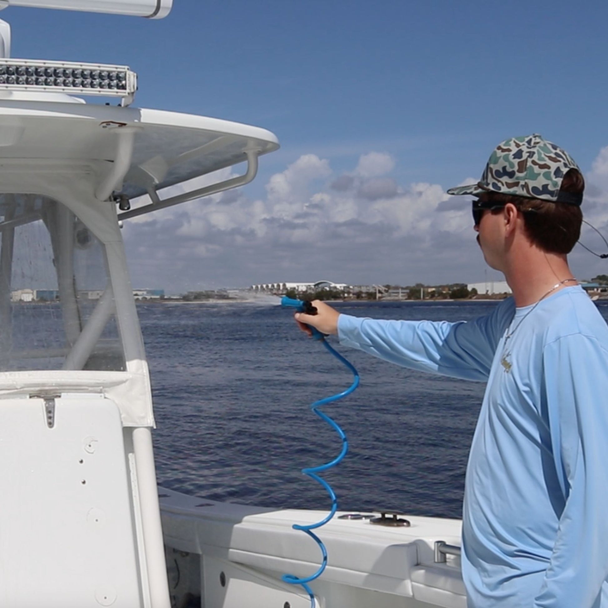 A man sprays a boat's T-top with a blue washdown hose.