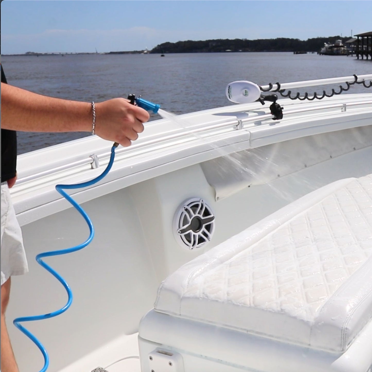 A man sprays boat vinyl with a blue coiled washdown hose and plastic nozzle.