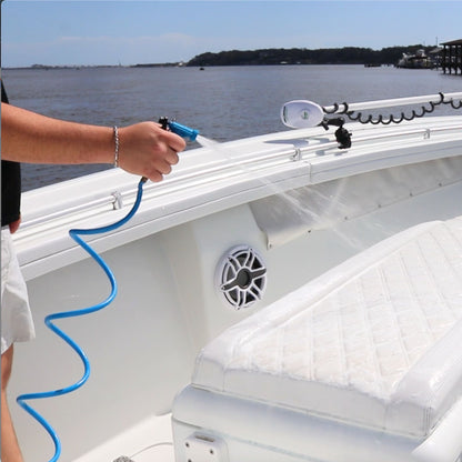 A man sprays boat vinyl with a blue coiled washdown hose and plastic nozzle.
