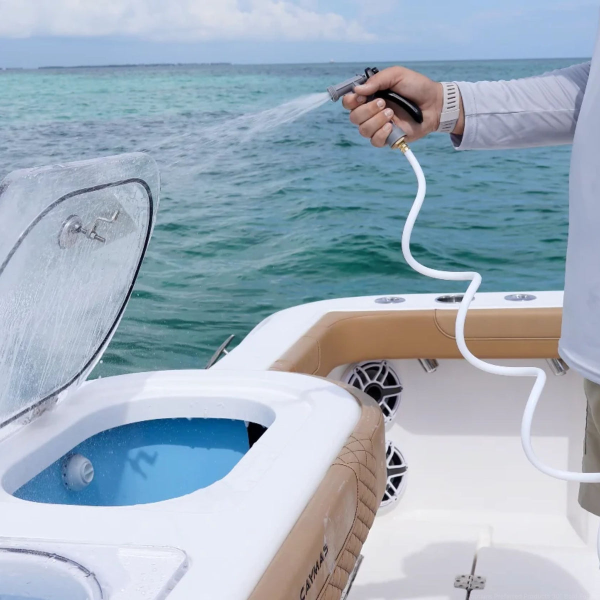 A man sprays a white washdown hose with gray nozzle to wash off a boat.