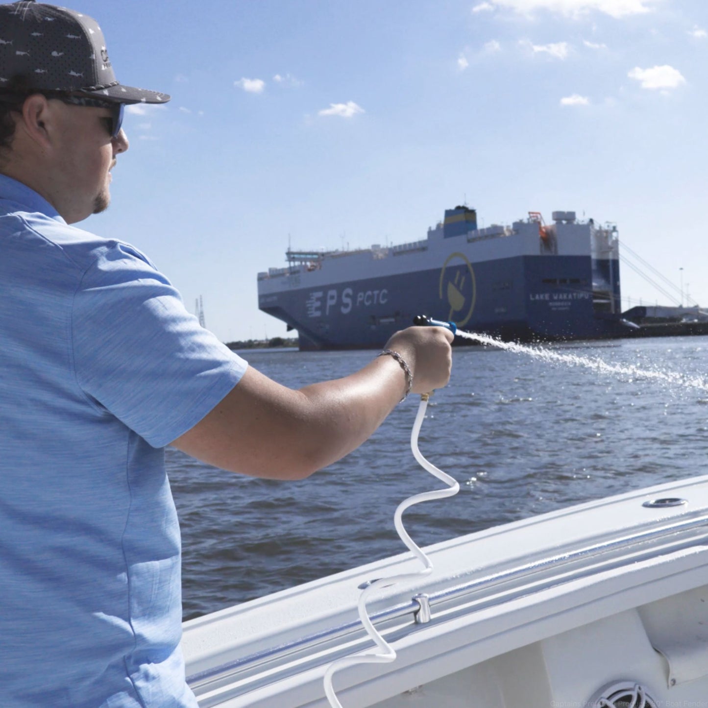 Man spraying down a boat with a white  coiled washdown hose.