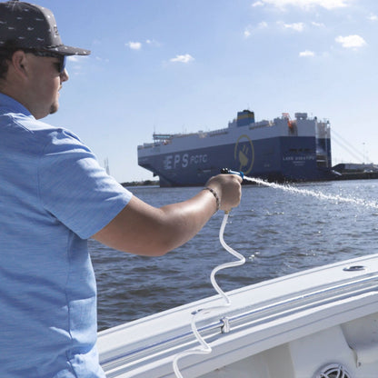 Man spraying down a boat with a white  coiled washdown hose.