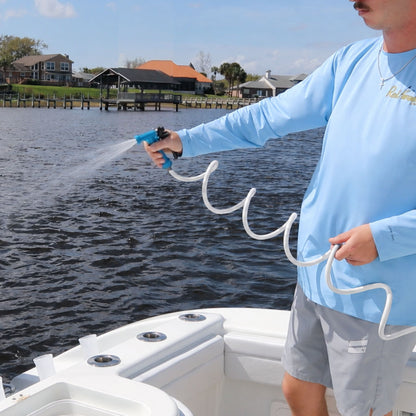 A man sprays a white boat hose to rinse his boat on the water.